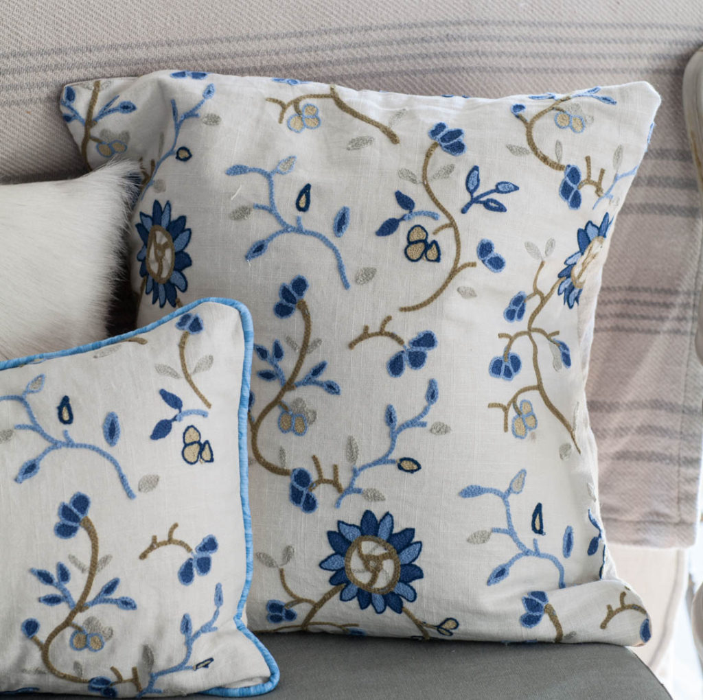 WHite and blue pillows accent a white linen couch placed in a white and  gray living room in front of a glass-paneled door f…